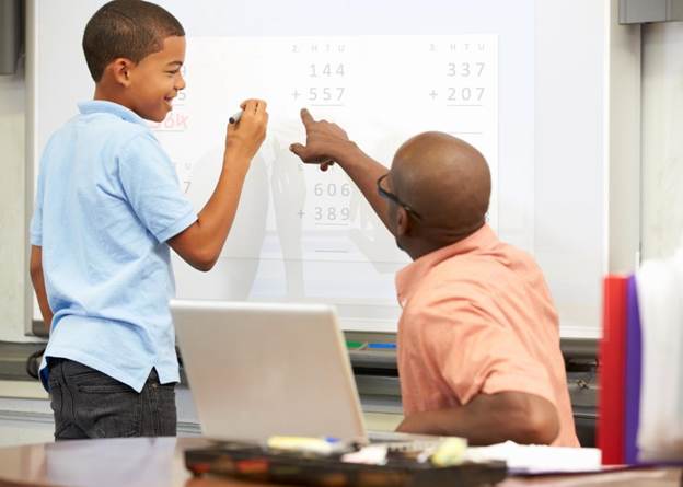 Elementary teacher points at board where child is writing