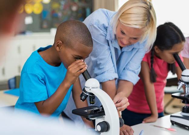 Elementary school teacher helps student with microscope