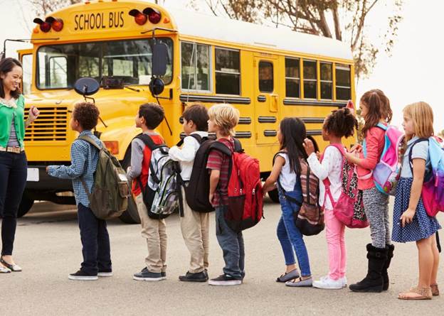 Elementary aged kids wait for school bus with their teacher