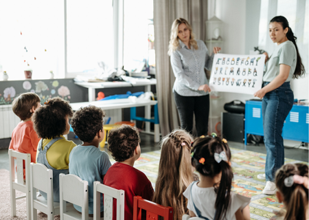 Two kindergarten teachers holding an alphabet poster for students